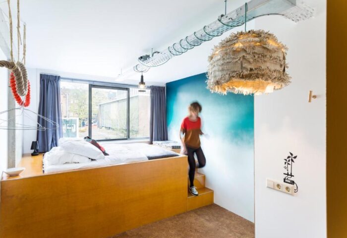 Ecomama Hotel room with raised bed, unique lighting, and a person descending steps. Gay-friendly hotel design for modern travelers.