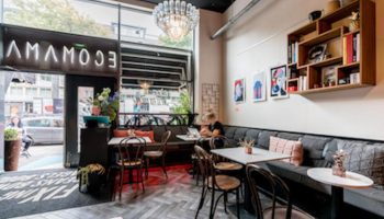 Ecomama Hotel's interior. Gay-friendly hotel with stylish decor, tables, chairs, and a cozy seating area. A chandelier adds a touch of elegance.