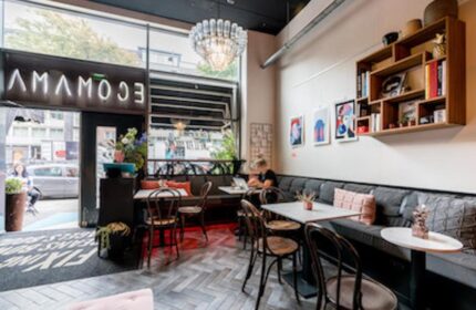 Ecomama Hotel's interior. Gay-friendly hotel with stylish decor, tables, chairs, and a cozy seating area. A chandelier adds a touch of elegance.