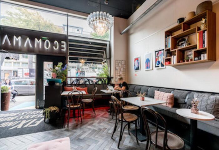 Ecomama Hotel's interior. Gay-friendly hotel with stylish decor, tables, chairs, and a cozy seating area. A chandelier adds a touch of elegance.