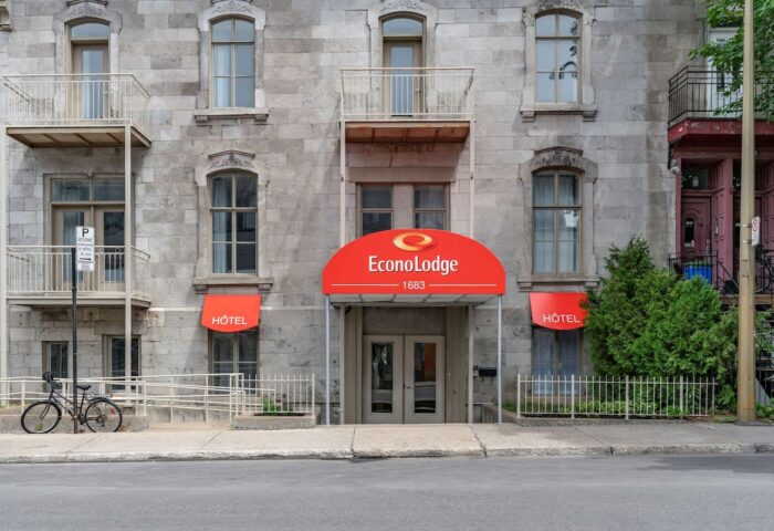 Econo Lodge hotel exterior. Gay-friendly travel lodging with red awning. Building facade with windows, balconies, and hotel signage.