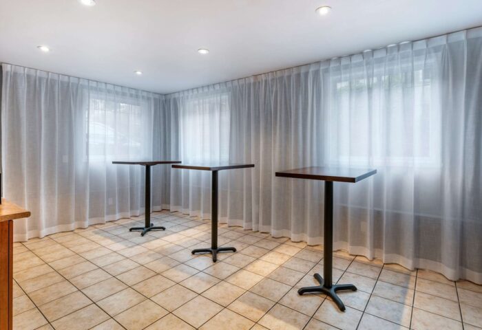 Econo Lodge gay-friendly hotel event space. Three tables stand in front of sheer curtains and windows, providing a modern, versatile area.