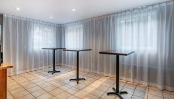 Econo Lodge gay-friendly hotel event space. Three tables stand in front of sheer curtains and windows, providing a modern, versatile area.