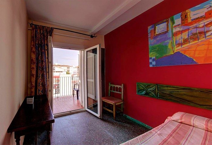 El Cid Gay-Friendly Hotel room with balcony. Red wall, painting, chair, and bed. Gay travel advice for a comfortable stay.