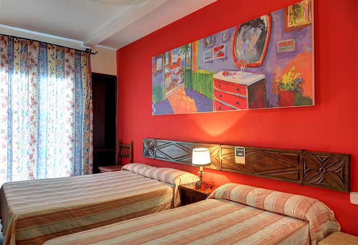 El Cid gay-friendly hotel room. Two beds with striped linens, red wall, painting above headboard. Gay travel lodging.