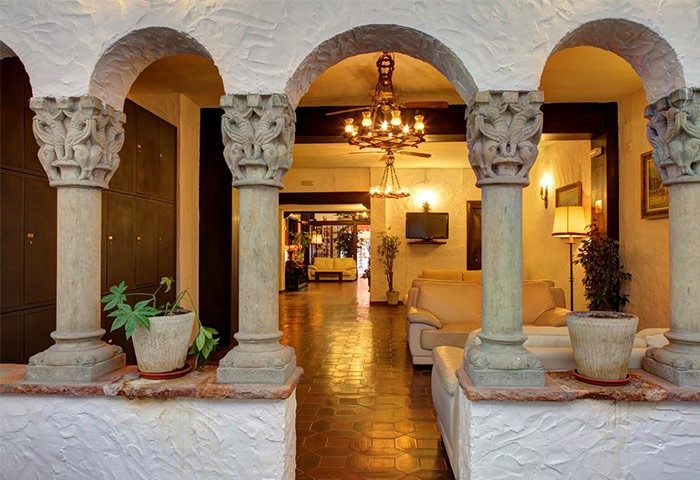 El Cid Gay-Friendly Hotel: Arched entrance with ornate pillars, leading to a warmly lit lobby with sofas. Welcoming space for gay travelers.