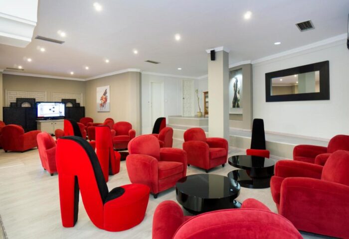 El Pozo, gay-friendly hotel lounge. Red armchairs & stiletto heel chairs. Modern design, black tables, TV. Stylish gay travel space.