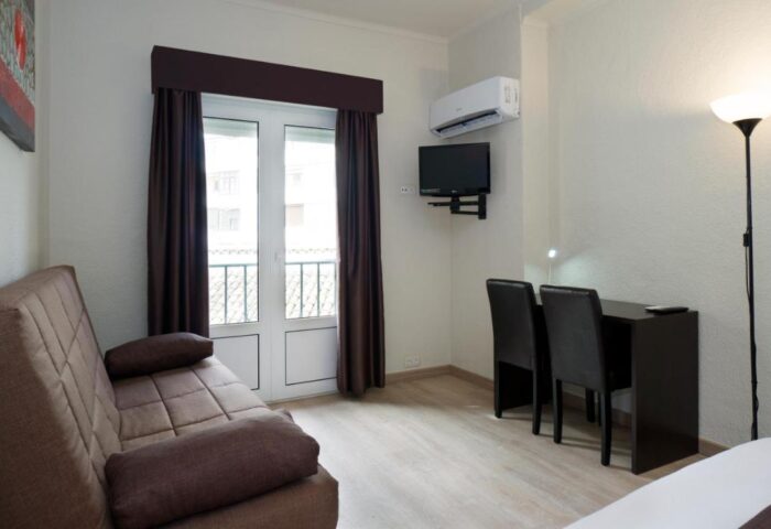 El Pozo Gay-Friendly Hotel room interior. Features a sofa, desk, chairs, TV, air conditioning, and balcony, offering comfortable gay travel.