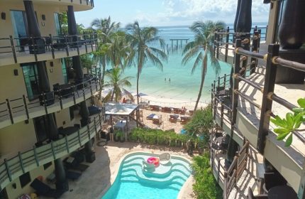 El Taj Oceanfront Condo Hotel view. Beachside gay-friendly hotel with pool, palm trees, and ocean view in Playa del Carmen, Mexico.