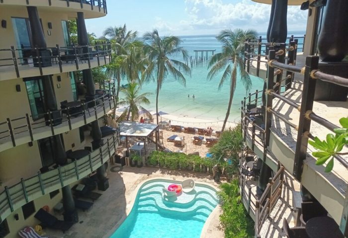 El Taj Oceanfront Condo Hotel view. Beachside gay-friendly hotel with pool, palm trees, and ocean view in Playa del Carmen, Mexico.