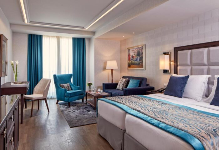 Electra Metropolis Hotel's gay-friendly room. Modern interior with blue accents, including curtains, armchair, sofa, and bed runner.