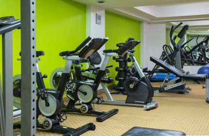 Empire Suites gay-friendly hotel gym. Exercise equipment includes stationary bikes, treadmills, weights, and a bench. Green wall.