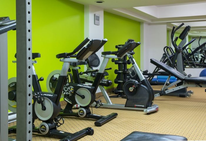 Empire Suites gay-friendly hotel gym. Exercise equipment includes stationary bikes, treadmills, weights, and a bench. Green wall.