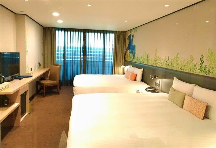 Energy Inn: Gay-friendly hotel room with two beds, desk, TV, and a nature-themed mural. Comfortable stay for gay travelers.