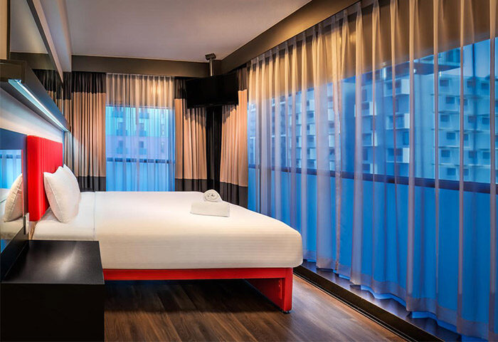 Essence Hotel Carlton room. Gay-friendly hotel with red bed frame, white linens, and sheer curtains. Modern design for gay men travel.