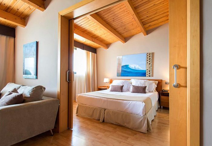 Estela Barcelona gay-friendly hotel room. Interior view of a bedroom with a double bed, sofa, wooden ceiling, and artwork of a wave on the wall.