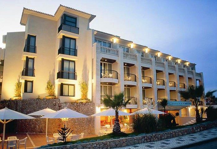 Estela Barcelona gay-friendly hotel. The exterior of the hotel features multiple balconies, palm trees, and outdoor seating with umbrellas.