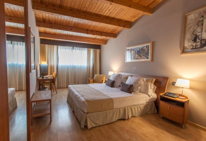 Estela Barcelona gay-friendly hotel room. Interior view of a bedroom with a wooden ceiling, a large bed, and warm lighting. Gay travel advice.