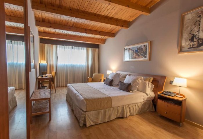 Estela Barcelona gay-friendly hotel room. Interior view of a bedroom with a wooden ceiling, a large bed, and warm lighting. Gay travel advice.