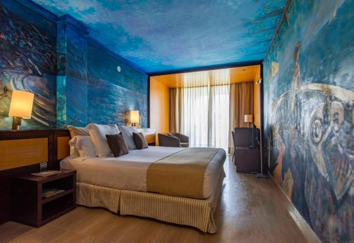 Estela Barcelona gay-friendly hotel room. Artistic blue wall mural, king bed, desk, and chairs. Ideal gay travel accommodation.