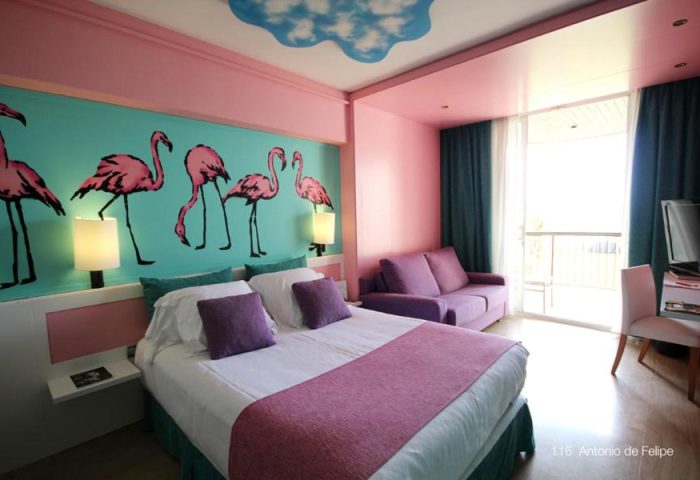 Estela Barcelona gay-friendly hotel room. Bedroom with flamingo wall art, pink accents, purple sofa, and balcony. Modern, stylish design.