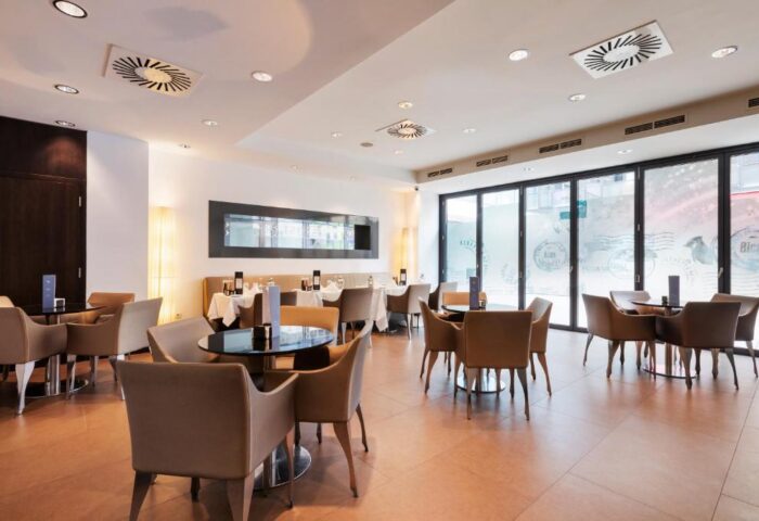 Eurostars Budapest Center gay-friendly hotel restaurant. Tables with beige chairs, black table tops, and large windows. Modern interior design.
