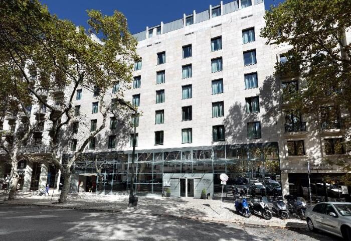 Eurostars Hotel das Letras, a gay-friendly hotel. Facade view of the hotel with trees, scooters, and cars in front. Lisbon gay travel.