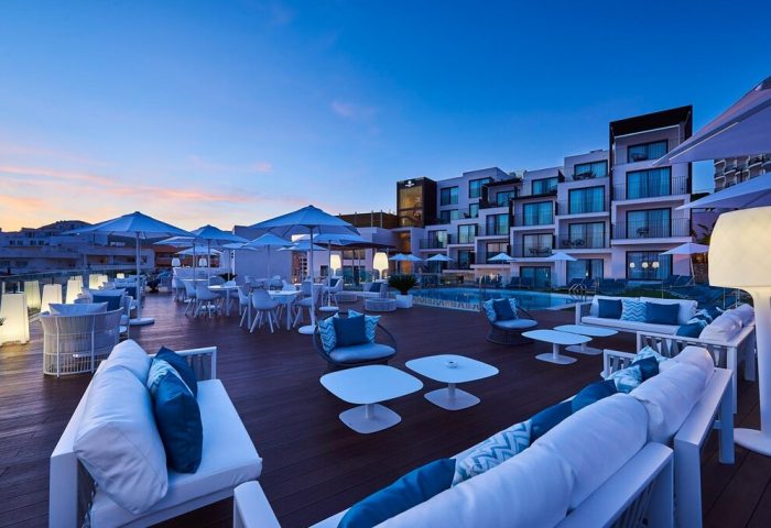 Eurostars Ibiza, a gay-friendly hotel. Outdoor pool area with white lounge furniture and umbrellas. Modern hotel architecture in Ibiza.