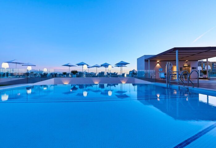Eurostars Ibiza gay-friendly hotel rooftop pool at dusk. Umbrellas, lounge chairs, and bar area visible. Perfect for gay travel in Ibiza.