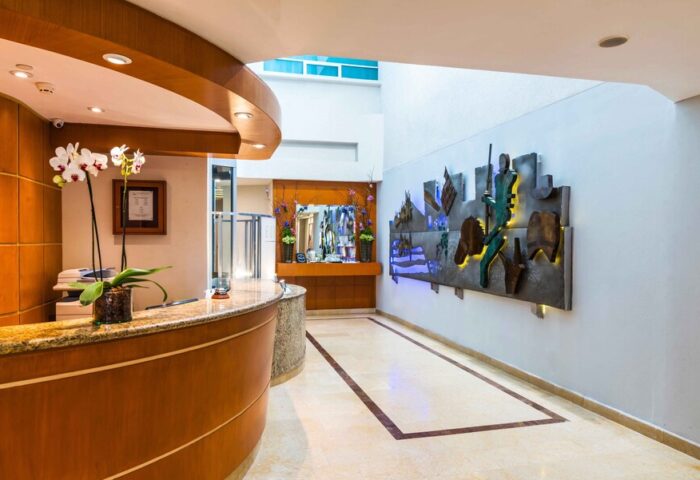 Eurostars Zona Rosa Suites lobby. Gay-friendly hotel with modern design, a reception desk with orchids, and an artistic wall feature. LGBT travel.