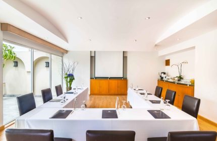 Eurostars Zona Rosa Suites gay-friendly hotel meeting room. U-shaped table with white tablecloth, brown chairs, and presentation screen.