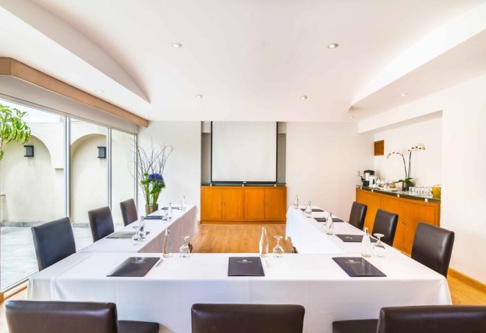 Eurostars Zona Rosa Suites gay-friendly hotel meeting room. U-shaped table with white tablecloth, brown chairs, and presentation screen.