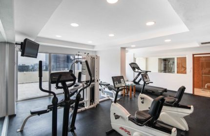 Eurostars Zona Rosa Suites gay-friendly hotel gym. Exercise equipment includes treadmills, stationary bikes, and weight machines. TV on wall.