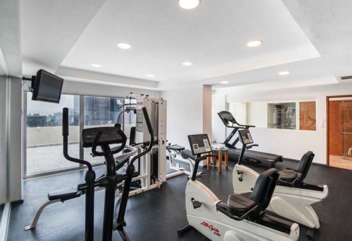 Eurostars Zona Rosa Suites gay-friendly hotel gym. Exercise equipment includes treadmills, stationary bikes, and weight machines. TV on wall.