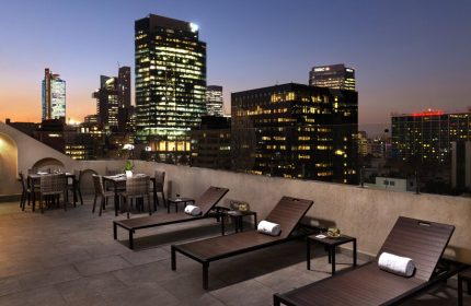Rooftop view at Eurostars Zona Rosa Suites, a gay-friendly hotel. Lounge chairs and dining tables overlook Mexico City's illuminated skyline.