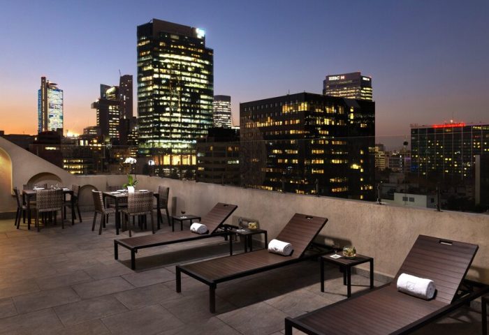 Rooftop view at Eurostars Zona Rosa Suites, a gay-friendly hotel. Lounge chairs and dining tables overlook Mexico City's illuminated skyline.