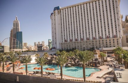 Excalibur Hotel pool view. Gay-friendly hotel in Las Vegas with palm trees, sun loungers, and a castle-themed building. Great for gay travel.