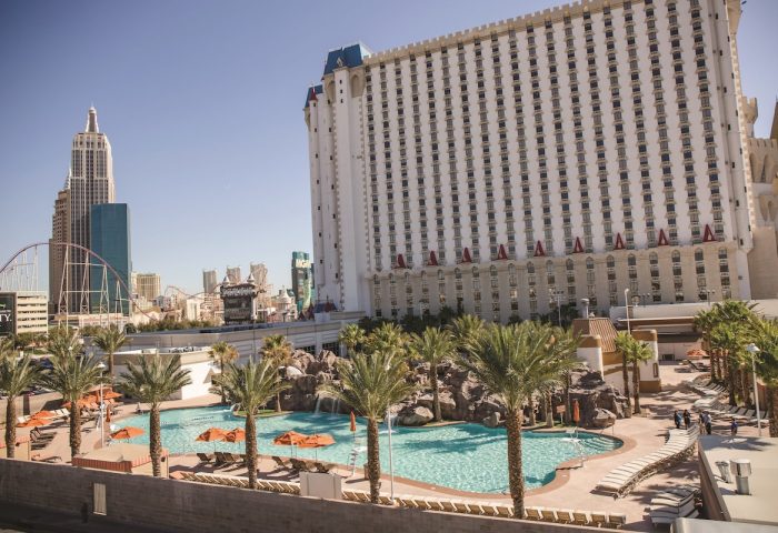 Excalibur Hotel pool view. Gay-friendly hotel in Las Vegas with palm trees, sun loungers, and a castle-themed building. Great for gay travel.
