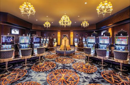 Excalibur Hotel's casino area. Slot machines line the walls, and chandeliers hang from the ceiling. Gay-friendly hotel with luxury decor.