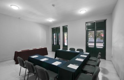 Exe Cities Reforma gay-friendly hotel meeting room. Tables set up in a U-shape with chairs around them. Windows with shutters in the background.