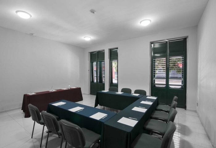 Exe Cities Reforma gay-friendly hotel meeting room. Tables set up in a U-shape with chairs around them. Windows with shutters in the background.