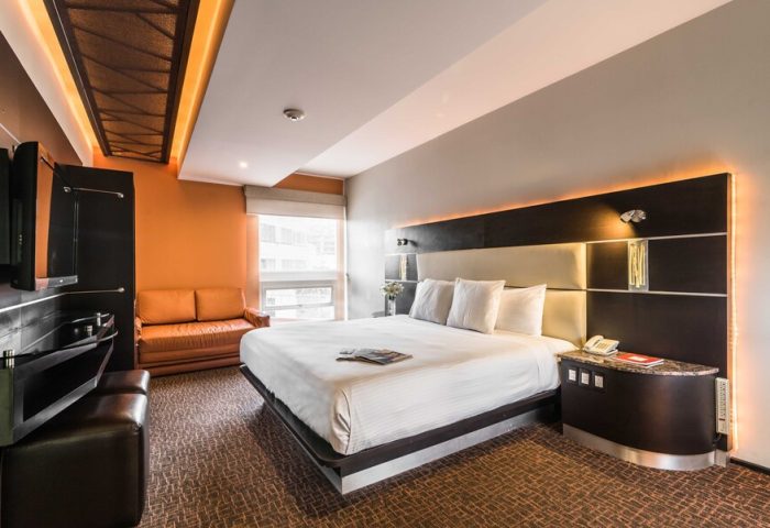 Exe Cities Reforma gay-friendly hotel room. Modern design, king bed, orange accent wall, and sofa. Ideal for gay travelers in Mexico City.