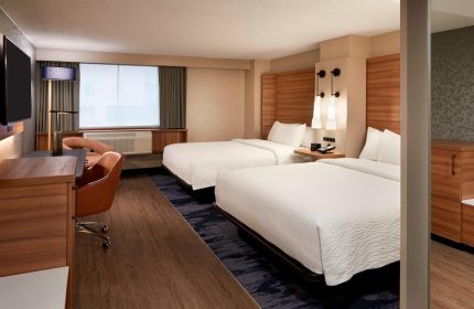 Fairfield by Marriott Montreal Downtown hotel room. Two beds with white linens, desk, chair, and modern lighting. Gay-friendly hotel.