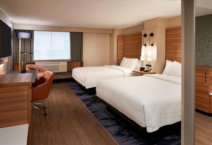 Fairfield by Marriott Montreal Downtown hotel room. Two beds with white linens, desk, chair, and modern lighting. Gay-friendly hotel.