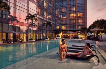 Fairmont Makati gay-friendly hotel pool view. Couple relaxing by the pool with drinks. Luxury travel in Makati, Philippines.