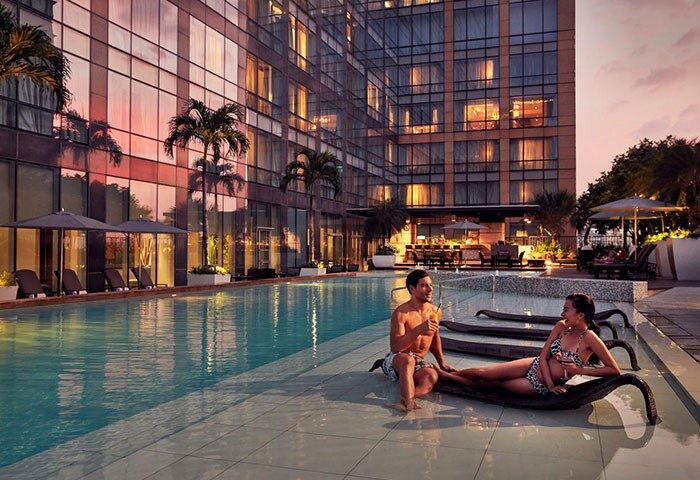 Fairmont Makati gay-friendly hotel pool view. Couple relaxing by the pool with drinks. Luxury travel in Makati, Philippines.