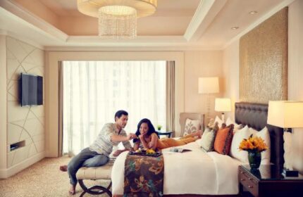 Gay-friendly Fairmont Makati hotel room. Couple enjoying breakfast in bed. Luxury travel experience in the Philippines. Modern design with warm lighting.