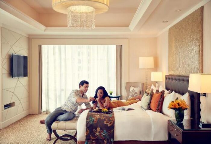 Gay-friendly Fairmont Makati hotel room. Couple enjoying breakfast in bed. Luxury travel experience in the Philippines. Modern design with warm lighting.