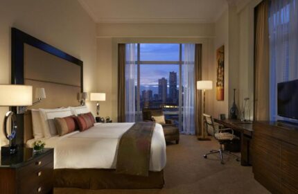 Fairmont Makati hotel room. Gay-friendly hotel with skyline view. Comfortable bed, desk, and city lights. Luxury travel in Makati, Philippines.