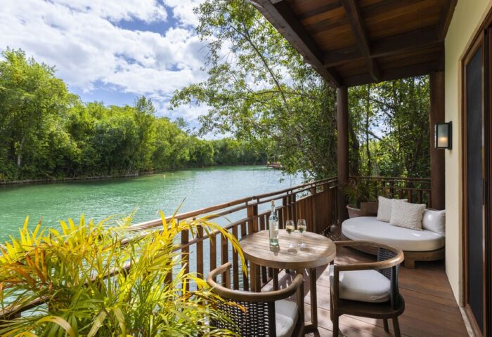 Fairmont Mayakoba gay-friendly hotel balcony view. Table with wine, chairs, and daybed overlook the lagoon. A relaxing gay travel destination.
